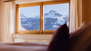 Een kamer met een bed en een raam met uitzicht op besneeuwde bergen.