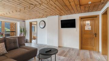 Un salon moderne avec un plafond en bois, un canapé, une table basse, un téléviseur et une porte.