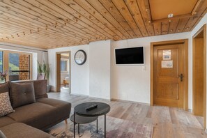 A modern living room with a wooden ceiling, a sofa, a coffee table, a TV, and a door.