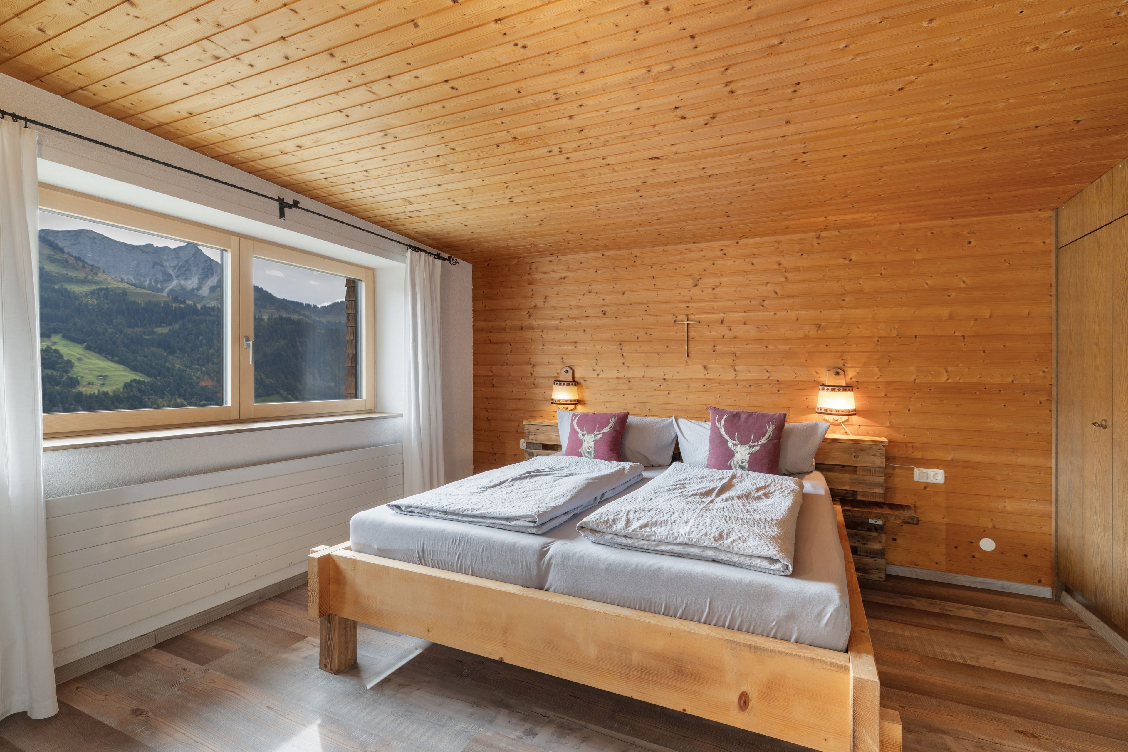 A wooden-paneled bedroom with a bed, two bedside lamps, and a window with a mountain view.