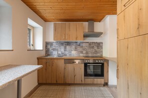 A compact kitchen with wooden cabinets, a built-in oven, and a stone backsplash.