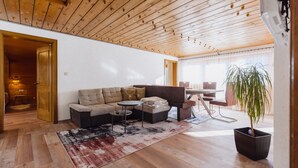 Een moderne woonkamer met een houten plafond, een hoekbank, een kleine ronde tafel en een potplant.