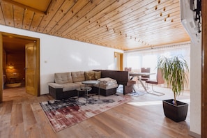 Un salon moderne avec un plafond en bois, un canapé d’angle, une petite table ronde et une plante en pot.