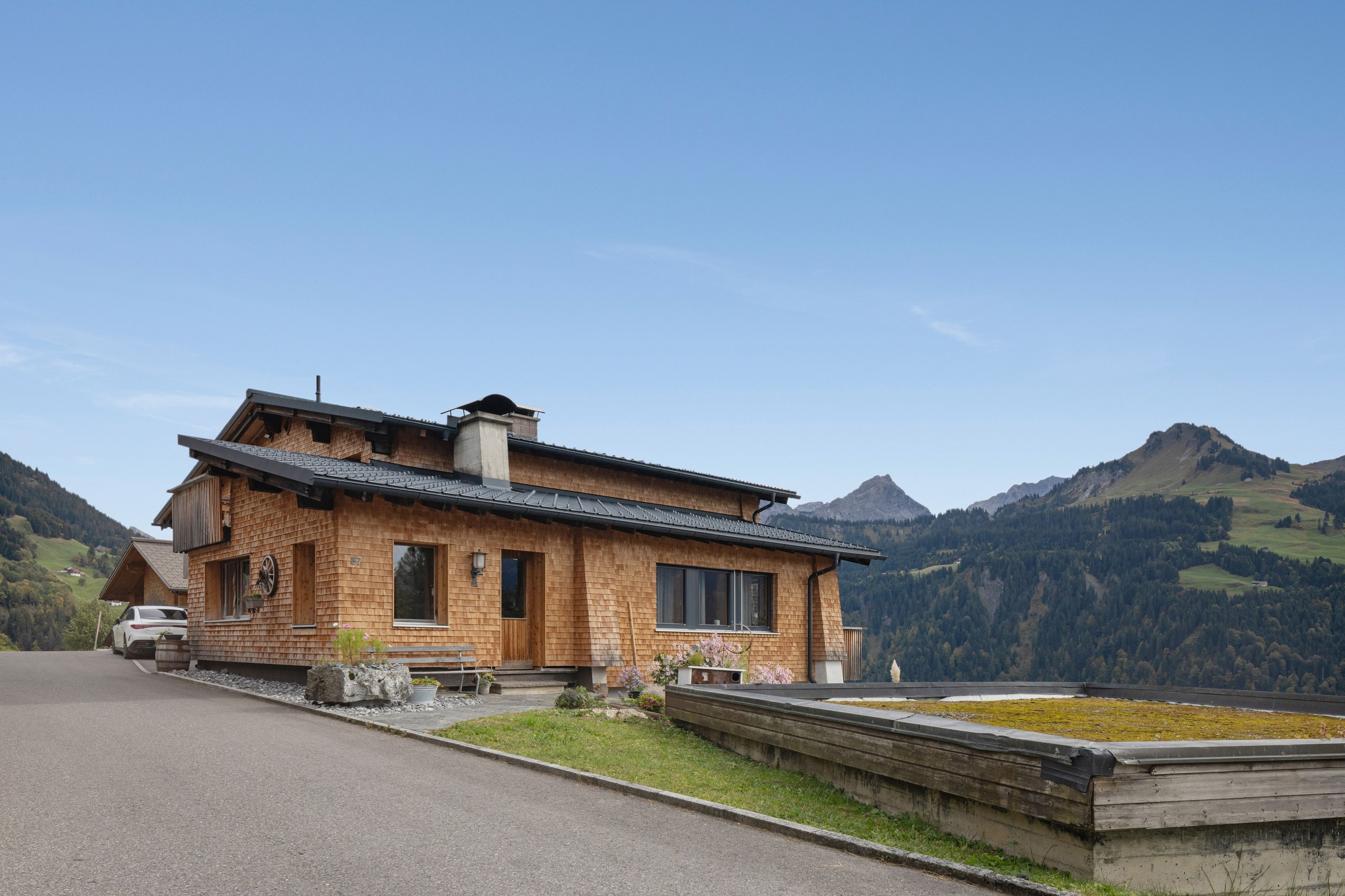 Une maison en bois avec un toit en pente, une cheminée et une vue sur les montagnes en arrière-plan.