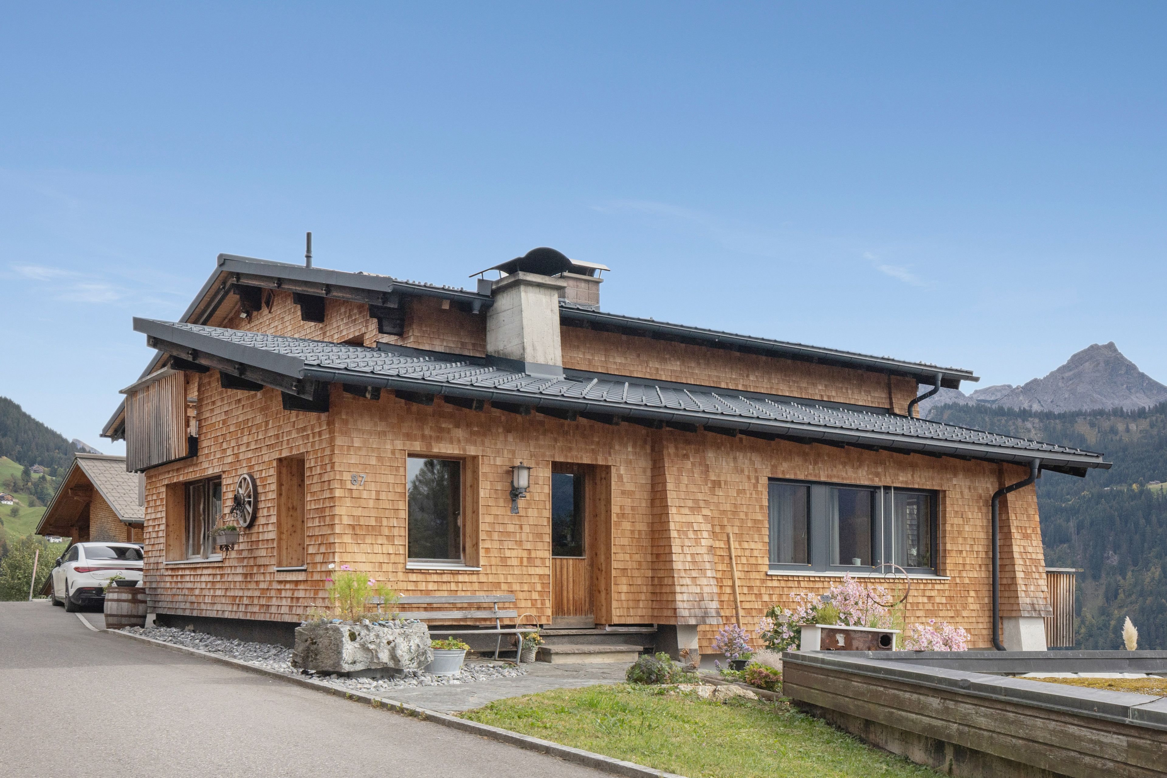 Une maison en bois à deux étages, avec un toit en pente, de grandes fenêtres et des fondations en pierre.