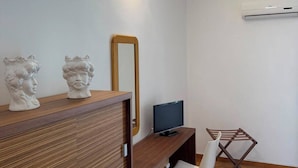 A modern room with a wooden desk, a television, a mirror, and a wall-mounted air conditioner.
