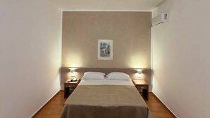 A single bed with a headboard, two bedside tables with lamps, a framed picture on the wall, and an air conditioning unit.