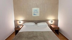A hotel room with a large bed, two bedside tables with lamps, a wall-mounted picture, and a wooden floor.
