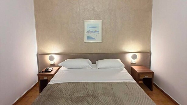 A hotel room with a large bed, two bedside tables with lamps, a wall-mounted picture, and a wooden floor.