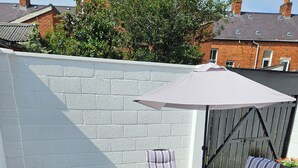 Une terrasse extérieure avec une table et des chaises, un pot de fleurs et une vue sur un bâtiment en briques.