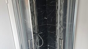 Une cabine de douche fermée par des parois en verre, équipée d’un pommeau de douche à main et d’un flexible de douche à main.