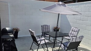 Une terrasse extérieure avec une table et des chaises, un barbecue et un mur blanc.
