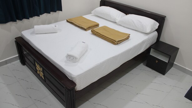 Una cama bien hecha con ropa de cama blanca y beige, un cabecero de madera y una mesita de noche pequeña con un cajón.