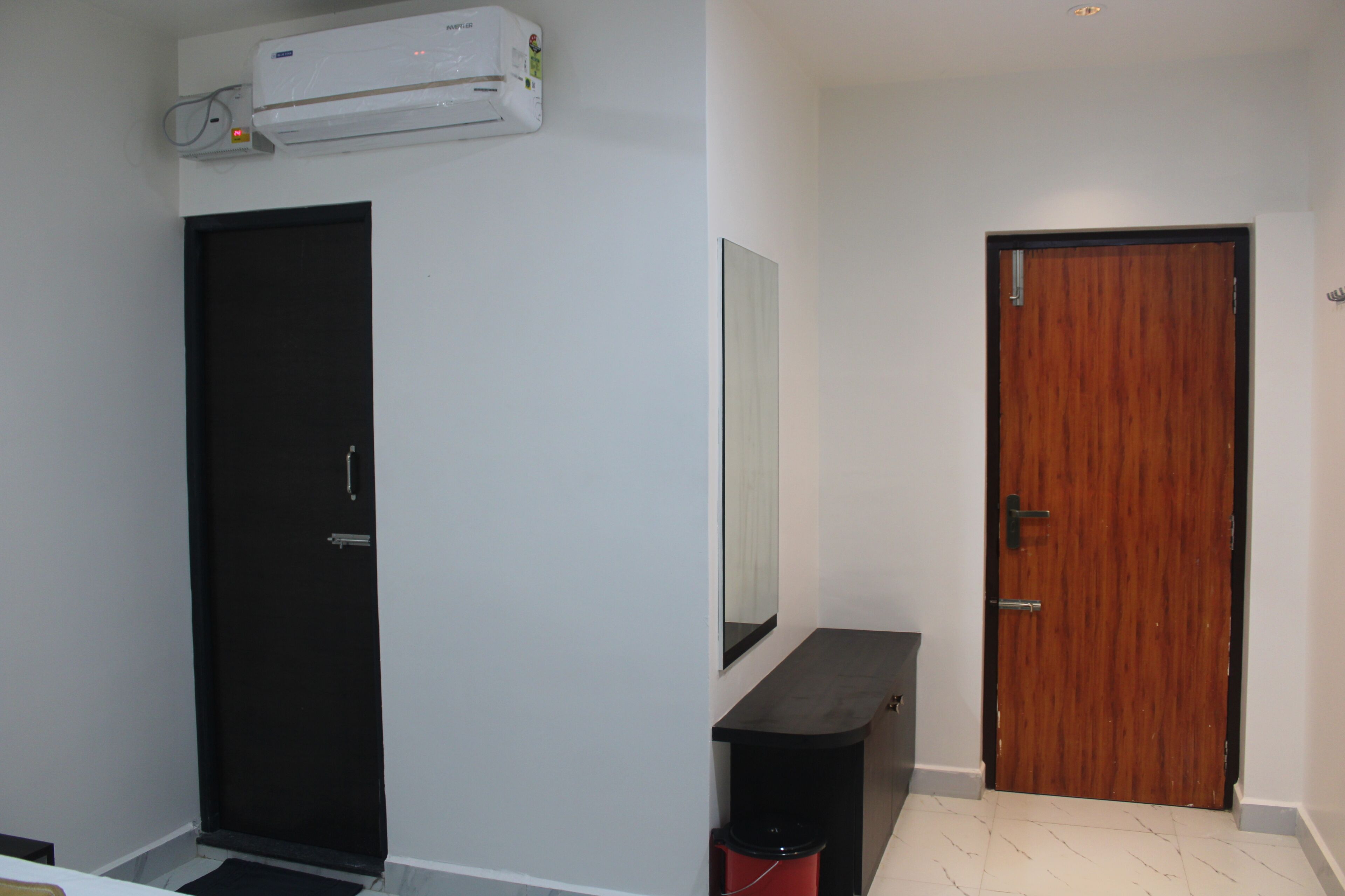 A room with a black door, a wooden door, a white wall, and a small black table.