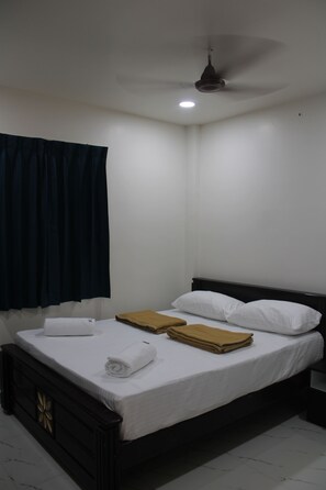 Una cama individual con ropa de cama blanca, cabecera oscura y ventilador de techo.