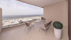 Un balcon avec vue sur la plage, une table, deux chaises et un pot de fleurs.