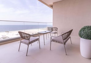 A balcony with a view of the beach, two wicker chairs, a small table, and a potted plant.