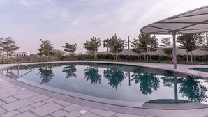 Une piscine à bord incurvé, entourée d’une zone pavée et d’arbres.