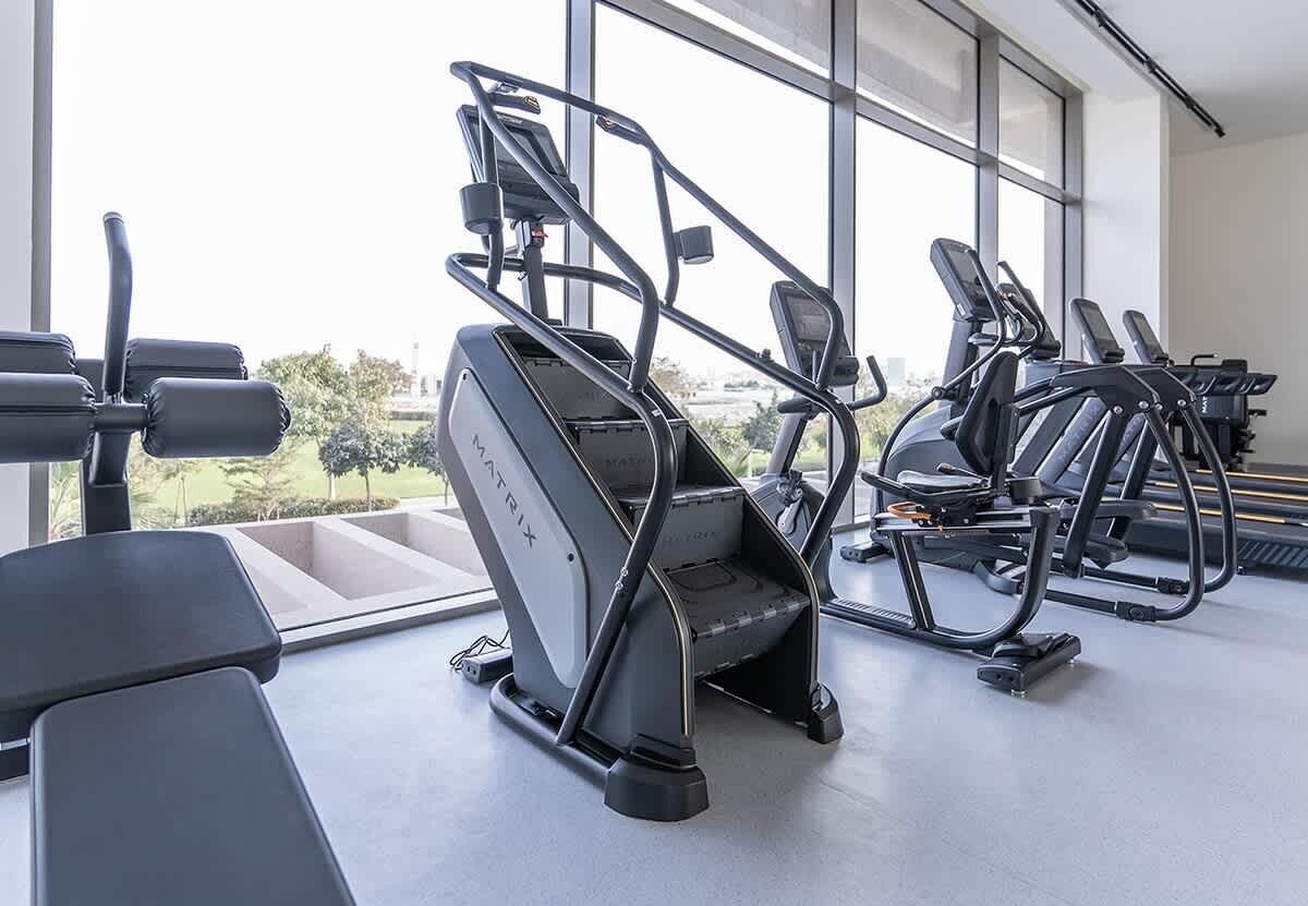 Uma academia com esteiras e equipamentos de exercício, grandes janelas e vista para o exterior.