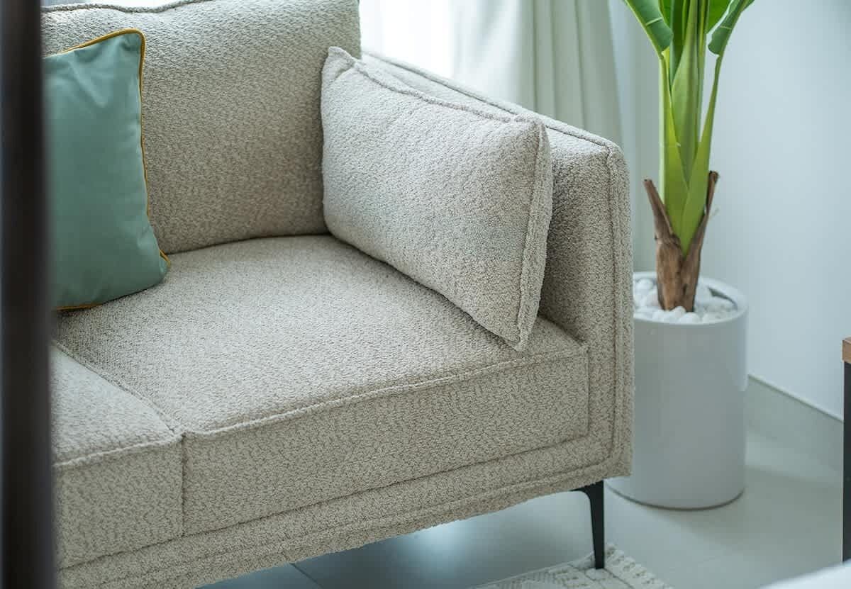 A beige sofa with a green pillow, a potted plant, and a white cylindrical object.