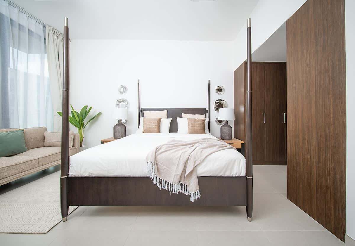 A modern bedroom with a four-poster bed, a sofa, a potted plant, and a wardrobe.