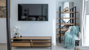 Ein modernes Wohnzimmer mit einem an der Wand befestigten Flachbildfernseher, einer Holzbank mit Stauraum, einem Hängeregal und einem Sessel mit Decke.