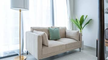 A beige sofa with a gold floor lamp, a green pillow, and a plant in a white room with a patterned rug.