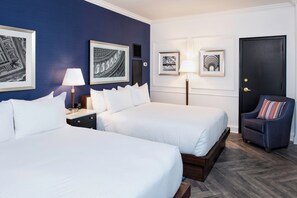 Hotellihuone, jossa on kaksi sänkyä, yöpöytä, tuoli ja seinillä on kehystettyjä kuvia.