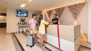 A reception area with a reception desk, a television screen, and a decorative wall. - d'primahotel Malioboro Yogyakarta (Yogyakarta)
