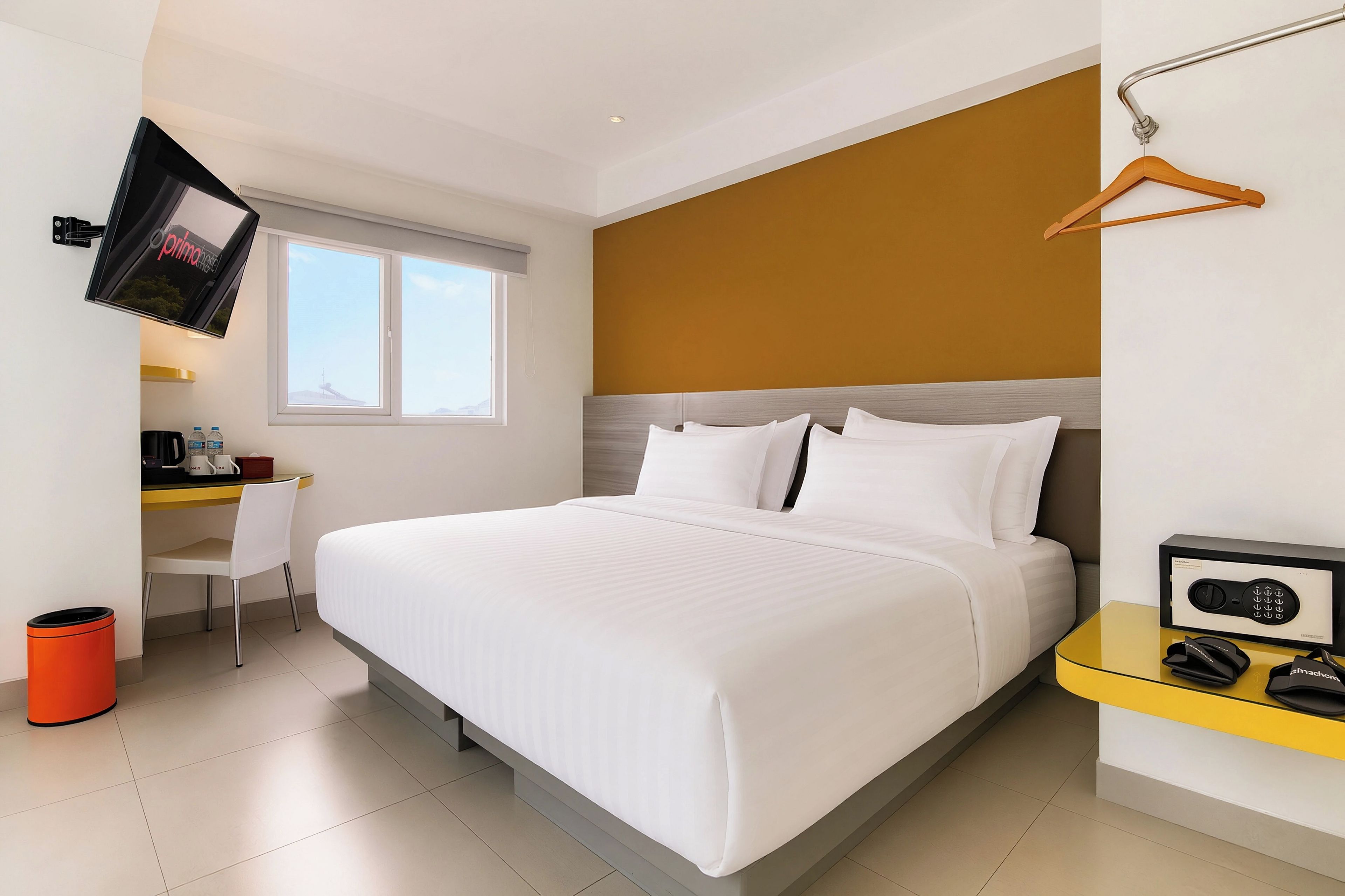 Habitación de hotel con cama, escritorio, silla, televisor montado en la pared y ventana.