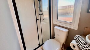 Et badeværelse med en glasafskærmet brusekabine, toilet og et vindue med persienner.