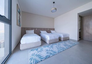 A modern hotel room with two beds, a large window, and a view of the city. - Blausee Beachfront Villa with Private Pool (Al Hamriyah)