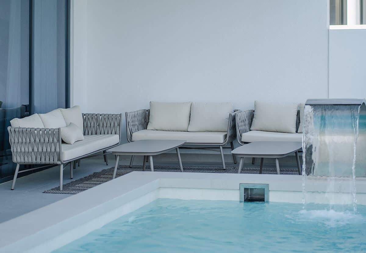 A poolside area with a sofa, lounge chairs, and a water feature.