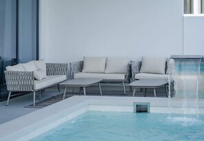 Ein Poolbereich mit einer Couch, Liegestühlen und einem Wasserspiel.