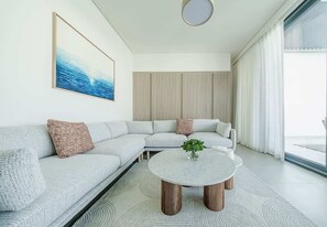 A modern living room with a sectional sofa, a round coffee table, and a large window with curtains. - Blausee Beachfront Villa with Private Pool (Al Hamriyah)