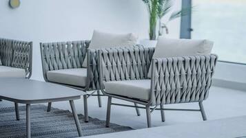 A modern outdoor seating area with woven chairs and a table, near a large window with a view.
