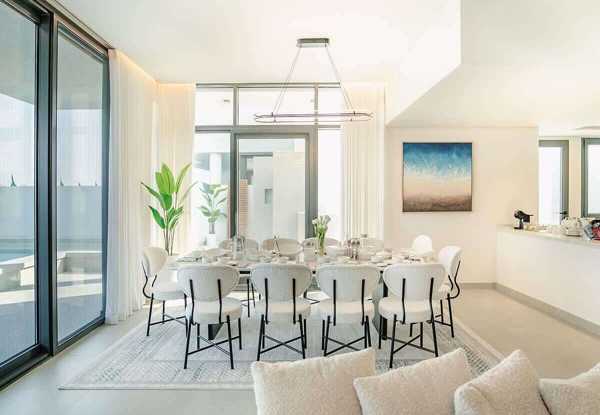 Uma sala de jantar moderna com divisória de vidro, mobiliário branco e um quadro na parede.
