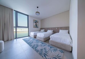 A hotel room with a large window, two beds, a painting, and a patterned rug.