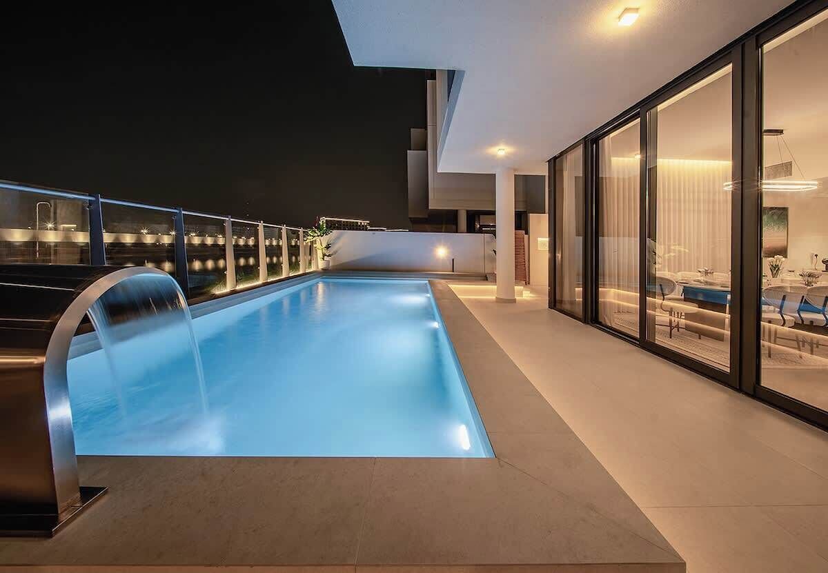 Una piscina moderna al aire libre con barandilla de cristal, un interior contemporáneo con zona de comedor y vistas despejadas del paisaje circundante.