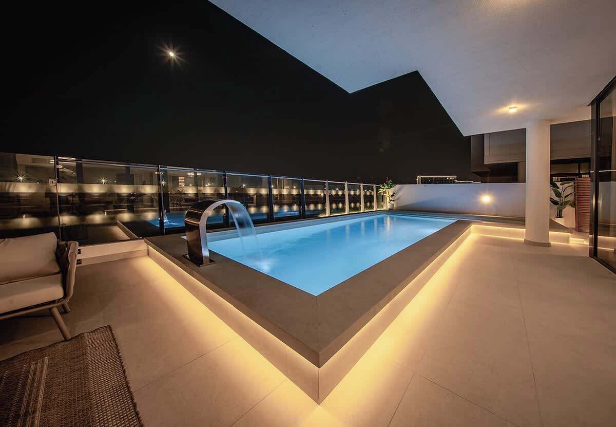 A modern indoor pool with a clear glass barrier, a lounge area with seating, and a contemporary architectural design.
