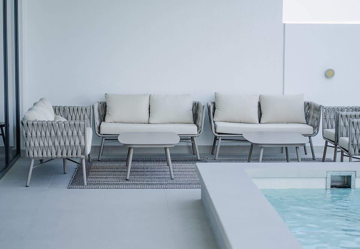 Uma área de estar moderna ao ar livre, com dois sofás brancos e uma mesa pequena, piscina e divisória de vidro.