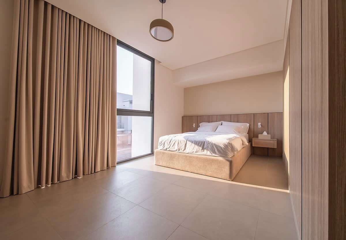Une chambre à coucher moderne avec un grand lit, une table de chevet et une vue sur l’extérieur, accessible par une porte coulissante.