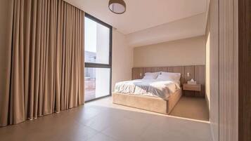 Une chambre à coucher moderne avec un grand lit, une table de chevet et une vue sur l’extérieur, accessible par une porte coulissante.