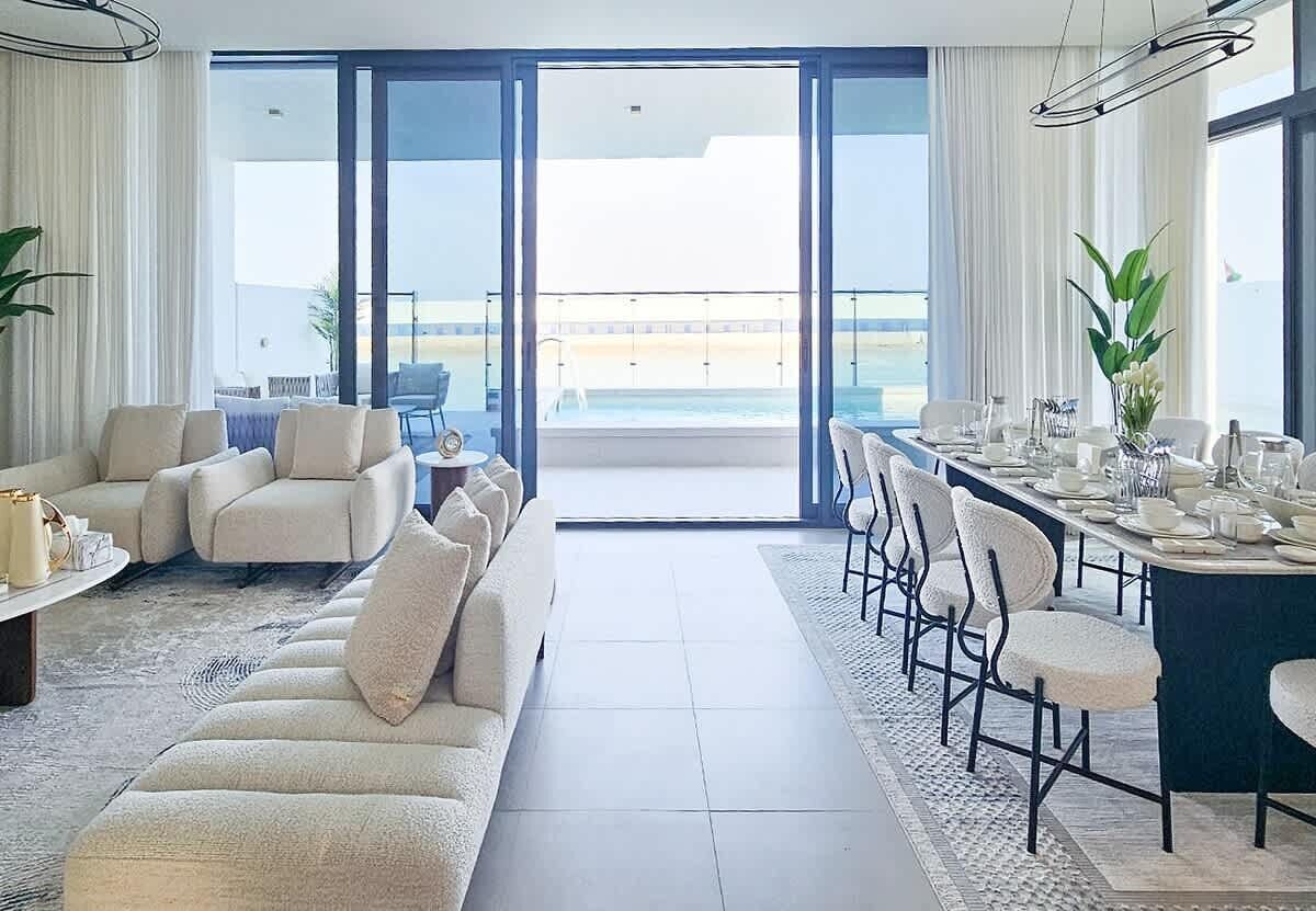 A spacious living area with a sofa set, a dining table set for four, and a view of the sea through large glass doors.