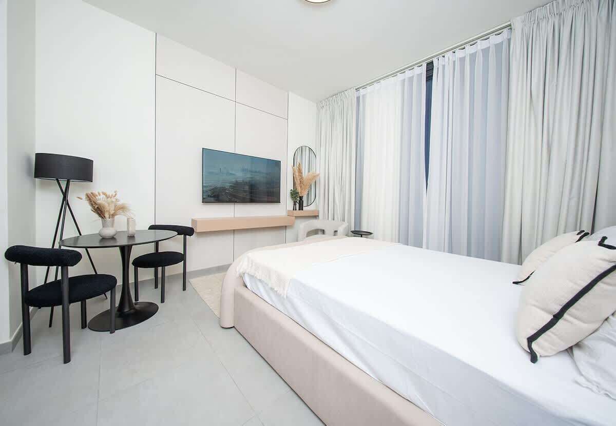 A modern hotel room with a bed, a desk with a chair, a lamp, and a painting on the wall.