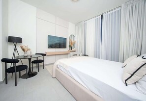 A modern hotel room with a bed, a desk with a chair, a lamp, and a painting on the wall.