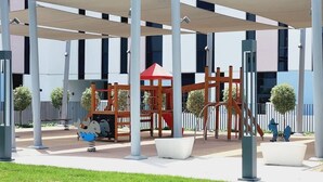 Ein Spielplatz mit einer Holzkonstruktion, einem roten Sonnensegel und einer weißen Bank.