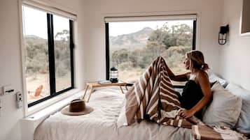 A bedroom with a large bed, a bedside table, a lamp, and a view of the outdoors.