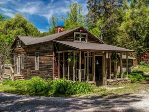 A rustic wooden cabin with a porch, a chimney, and a small garden area. - Historic Pioneer Cabin with Creek Views in Talking Rock, Georgia (Talking Rock)