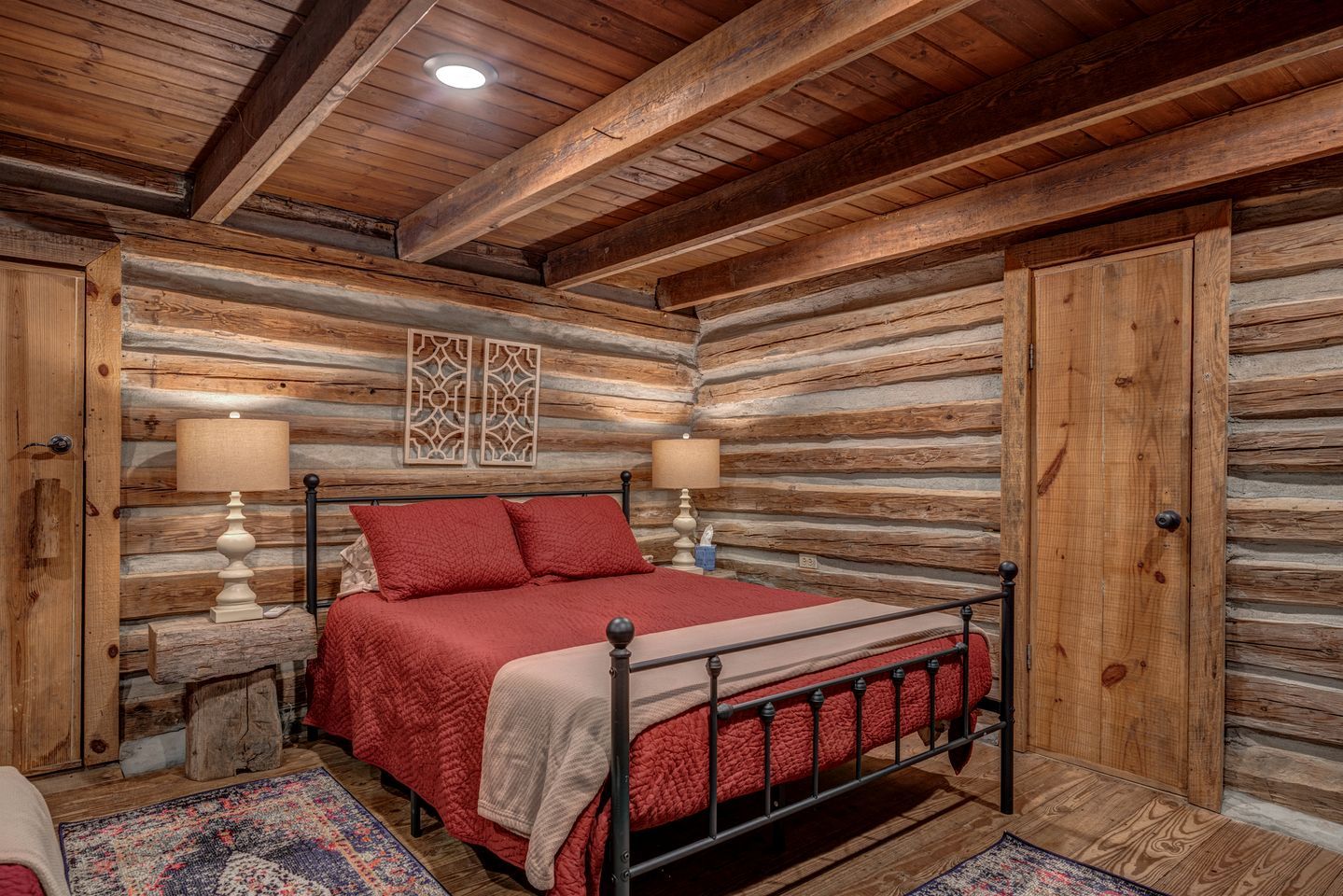 Un dormitorio tipo cabaña de madera con estructura de cama metálica, dos lámparas de noche y un panel decorativo en la pared.